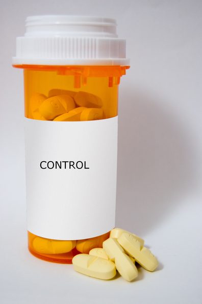 A standard orange prescription bottle full of yellow pills. The information on the label has been covered. A few pills sit outside the bottle, at its base.